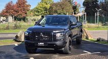 Schwarzer Mitsubishi L200 mit Offroad-Bereifung, Schnorchel und schwarzem Kühlergrill in schräger Frontansicht auf einem Parkplatz.