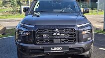 Schwarzer Mitsubishi L200 von vorne mit großem Kühlergrill, Mitsubishi-Emblem, geteilten Scheinwerfern und Frontstoßfänger.