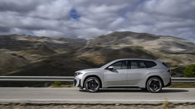 Seitenansicht des BMW iX3 der Neuen Klasse während der Fahrt vor bergiger Landschaft.