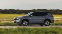 Seitenansicht eines Mitsubishi Outlander Plug-in-Hybrid während der Fahrt durch eine Landschaft.