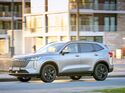 Silberner GWM Haval H6 in Seitenansicht während der Fahrt im städtischen Umfeld.