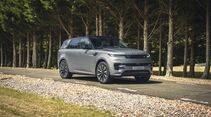 Silberner Range Rover Sport fährt auf einer asphaltierten Straße durch ein bewaldetes Gelände.