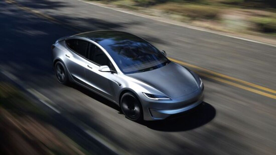 Silberner Tesla Model 3 fährt auf einer Landstraße, Seitenansicht aus erhöhter Perspektive.