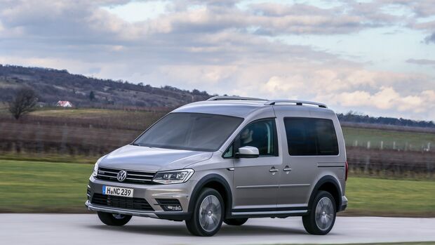 Silberner VW Caddy fährt auf einer Landstraße, umgeben von Feldern und leicht bewölktem Himmel