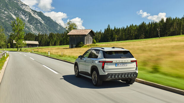 Skoda Epiq von hinten in Fahrt auf einer Landstraße vor einer Holzscheune in den Alpen.