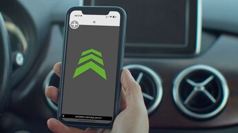Smartphone mit geoeffneter blitzer app in der hand eines fahrers im auto waehrend der navigation