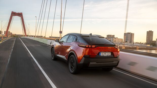 Subaru Uncharted 77 FWD Active in Orange bei der Fahrt auf einer Brücke, schräg von hinten fotografiert.