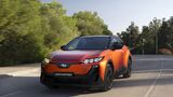 Subaru Uncharted 77 FWD Active in Orange bei der Fahrt auf einer Straße, schräg von vorn fotografiert.