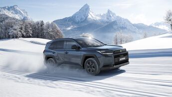 Suzuki Across SUV fährt auf verschneiter Straße in alpiner Landschaft, Seitenansicht mit Allradantrieb im Wintereinsatz.