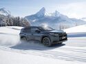 Suzuki Across SUV fährt auf verschneiter Straße in alpiner Landschaft, Seitenansicht mit Allradantrieb im Wintereinsatz.