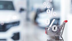 Symbolisches Einkaufswagensymbol mit Prozentzeichen vor unscharfen Elektrofahrzeugen, Darstellung von Preisentwicklung im Gebrauchtwagenmarkt.