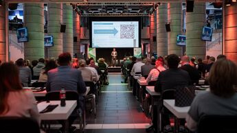 Teilnehmende sitzen in einem Konferenzsaal und verfolgen einen Vortrag auf der Bühne während der NaKoBeMo 2025.