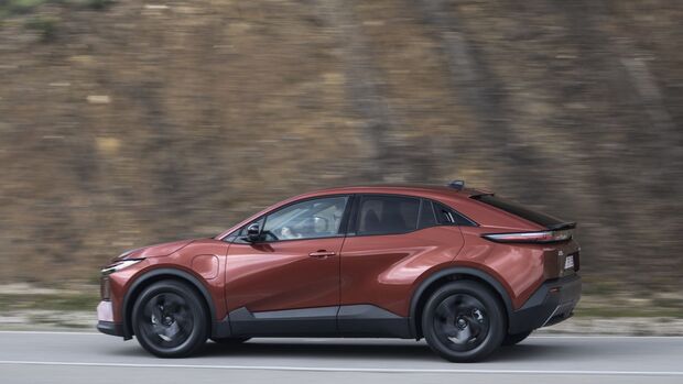 Toyota C-HR+ in Seitenansicht während der Fahrt entlang einer Felswand