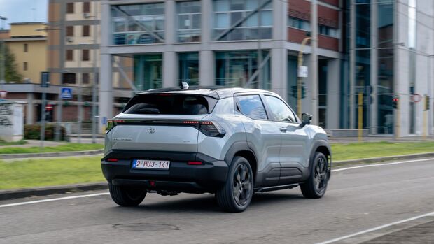 Toyota Urban Cruiser in Silber, Heckansicht, fährt auf einer Straße vor modernen Gebäuden.