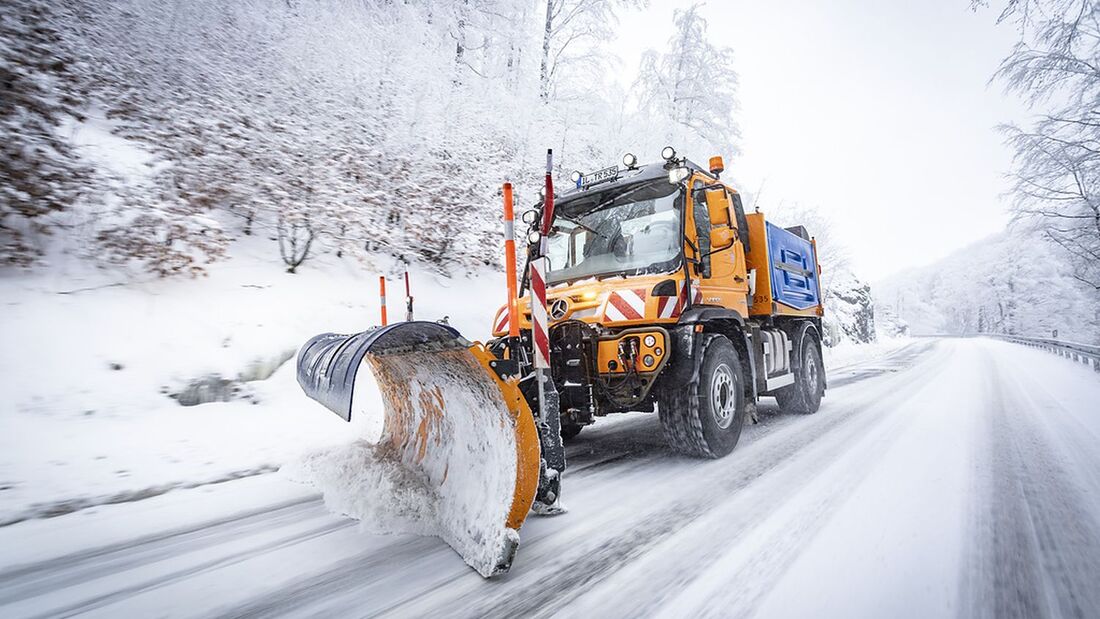 Unimog mit Schneepflug im Winterdiensteinsatz auf verschneiter Straße.