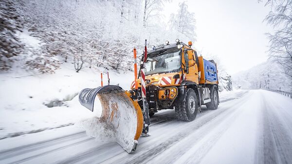 Unimog mit Schneepflug im Winterdiensteinsatz auf verschneiter Straße.