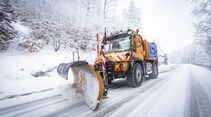 Unimog mit Schneepflug im Winterdiensteinsatz auf verschneiter Straße.