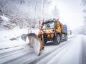 Unimog mit Schneepflug im Winterdiensteinsatz auf verschneiter Straße.