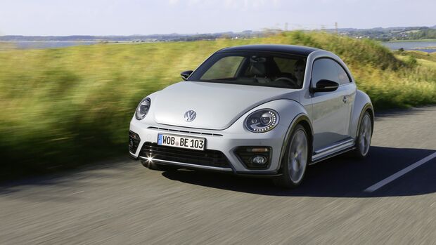 VW Beetle Coupe in Silber waehrend der Fahrt auf einer Landstrasse vor einer gruenen Landschaft.