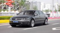VW Phaeton in Grau waehrend der Fahrt auf einer mehrspurigen Strasse vor staedtischer Kulisse.