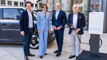 Vier Personen stehen vor einem VW ID. Buzz und einer Ladesaeule bei einem Termin zum Thema bidirektionales Laden.