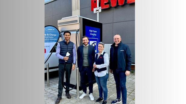 Vier Personen vor einer JOLT-Schnellladesaeule auf dem Parkplatz eines REWE-Markts in Heidelberg.
