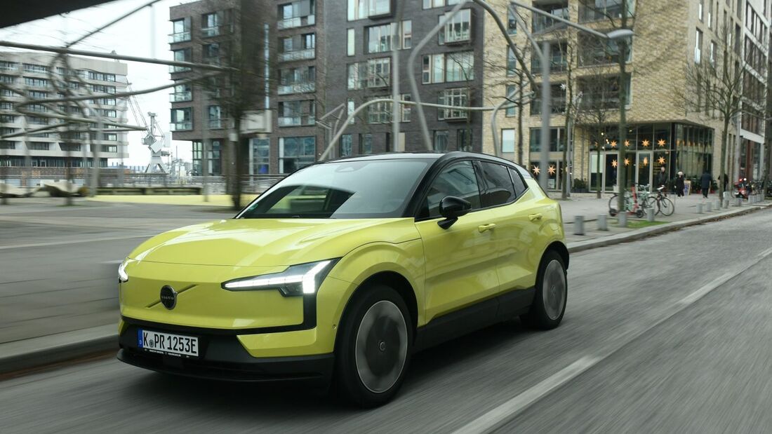 Volvo EX30 P8 AWD Electric in Gelb bei einer Fahraufnahme im Stadtverkehr, schräg von vorne fotografiert.
