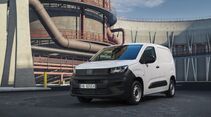 Weißer Fiat Doblò Professional Kastenwagen in Front-Seitenansicht vor einer Industrieanlage mit großen Rohrleitungen und Metallgeländern.