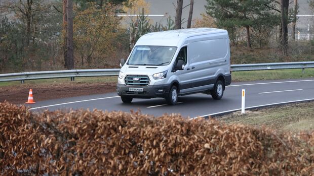Weißer Ford E-Transit fährt auf einer Teststrecke beim Ford Pro Leisure Experience Event in Lommel, mit Pylonen und Leitplanken.