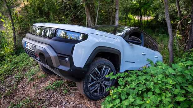 Weißer Jeep Compass 4xe fährt abseits eines befestigten Weges durch bewaldetes Gelände.