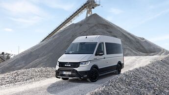 Weißer MAN TGE Transporter mit schwarzen Felgen auf einem Schotterweg in einer Kiesgrube vor einem Kiesberg und einer Förderbandanlage.