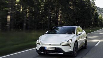 Weisser Polestar 4 faehrt auf Landstrasse durch bewaldete Landschaft