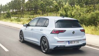 Weißer VW Golf Hybrid in Heckansicht während der Fahrt auf einer Landstraße mit Wald im Hintergrund.