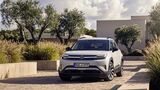 Weißer VW ID. Cross als Elektro-SUV in Front-Dreiviertelansicht auf einer gepflasterten Zufahrt vor einem modernen Gebäude.