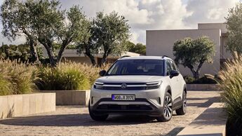 Weißer VW ID. Cross als Elektro-SUV in Front-Dreiviertelansicht auf einer gepflasterten Zufahrt vor einem modernen Gebäude.