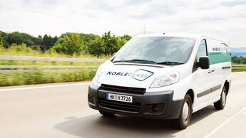 Weißer nobleglass-Transporter fährt auf der Straße, Front und Seitenlogo sichtbar, Einsatzfahrzeug im AFC-Risikomanagement.