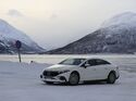 Weisses Elektroauto auf verschneiter Strasse vor winterlicher Berglandschaft und gefrorenem See. 