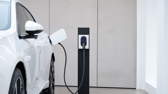 Weißes Elektroauto von Polestar lädt an einer Wandladestation in einem Innenraum.