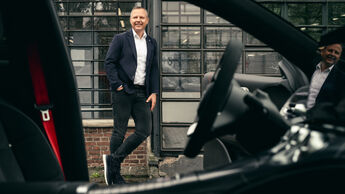 Wolfgang Ufer steht vor einem Industriegebäude, fotografiert durch den Innenraum eines Fahrzeugs.