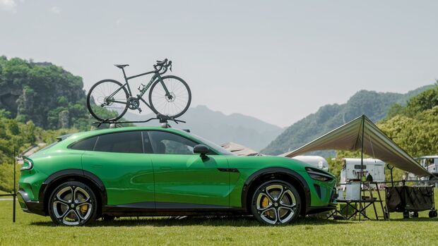 Xiaomi YU7 in Seitenansicht auf einer Wiese, mit Fahrrad auf dem Dachträger und Camping-Setup im Hintergrund.