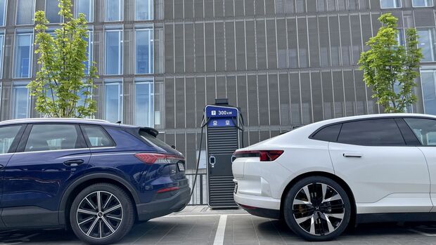 Zwei Elektrofahrzeuge stehen an einer Schnellladestation auf einem Unternehmensparkplatz vor einem Bürogebäude