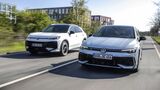 Zwei Volkswagen Modelle Golf und T-Roc Hybrid fahren nebeneinander auf einer Straße in urbaner Umgebung