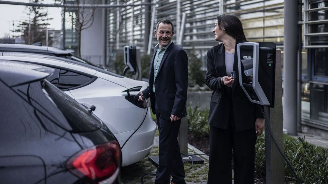 zwei personen laden elektroautos an ladestation auf firmenparkplatz