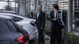 zwei personen laden elektroautos an ladestation auf firmenparkplatz